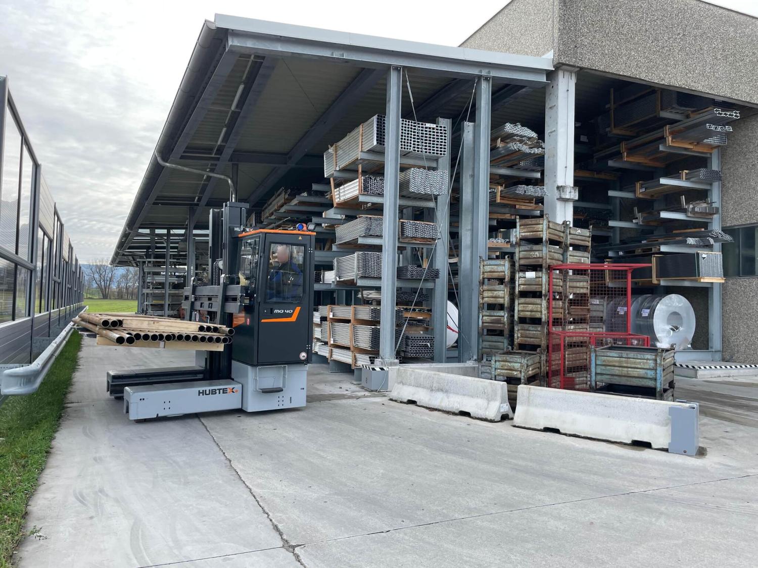 HUBTEX MQ40 PHOENIX meerwegheftruck transporteert metalen buizen bij buitenopslag