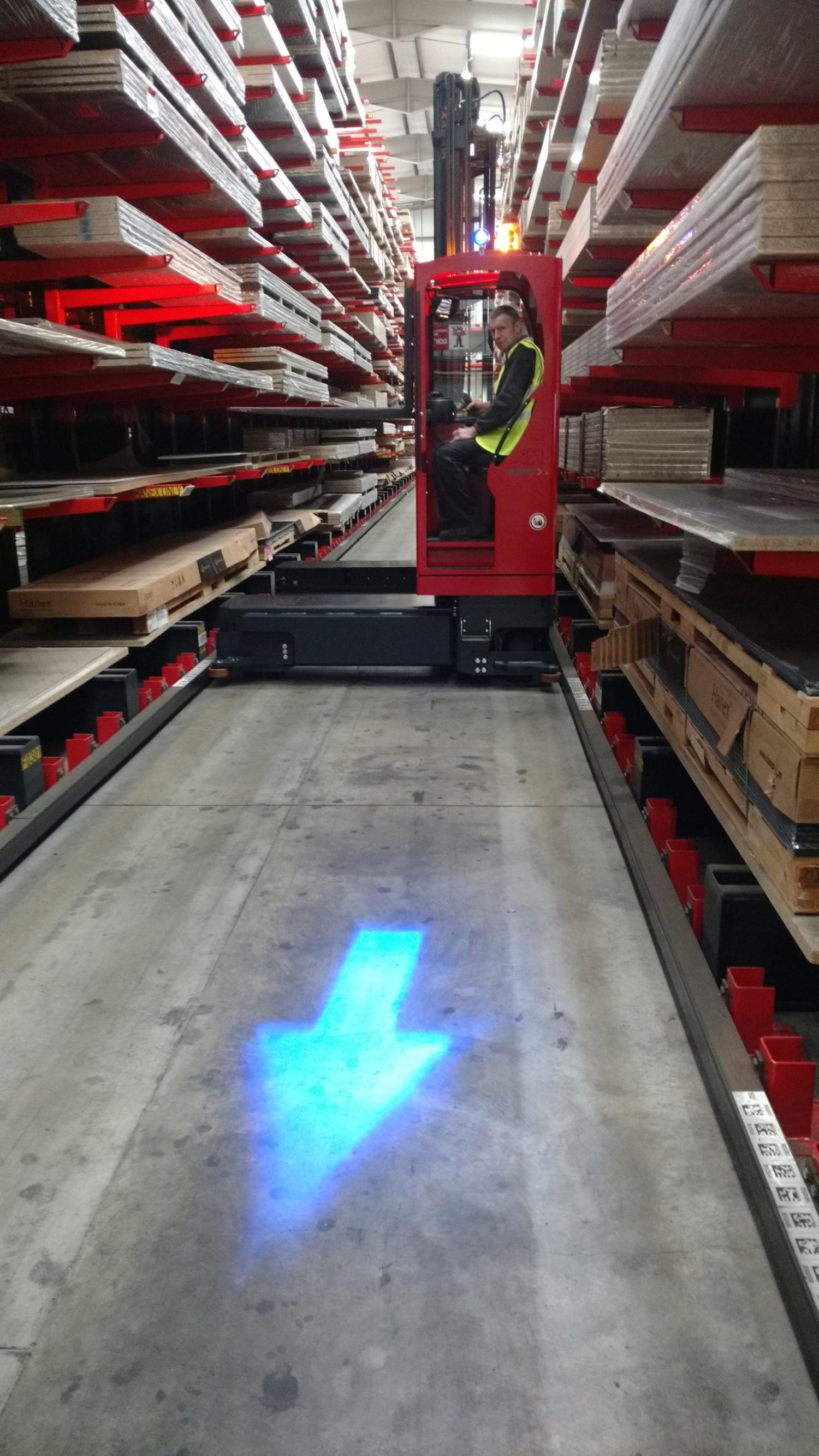 HUBTEX zijlader rijdt door smalle magazijngang met veiligheidsprojectie van blauwe pijl op de vloer