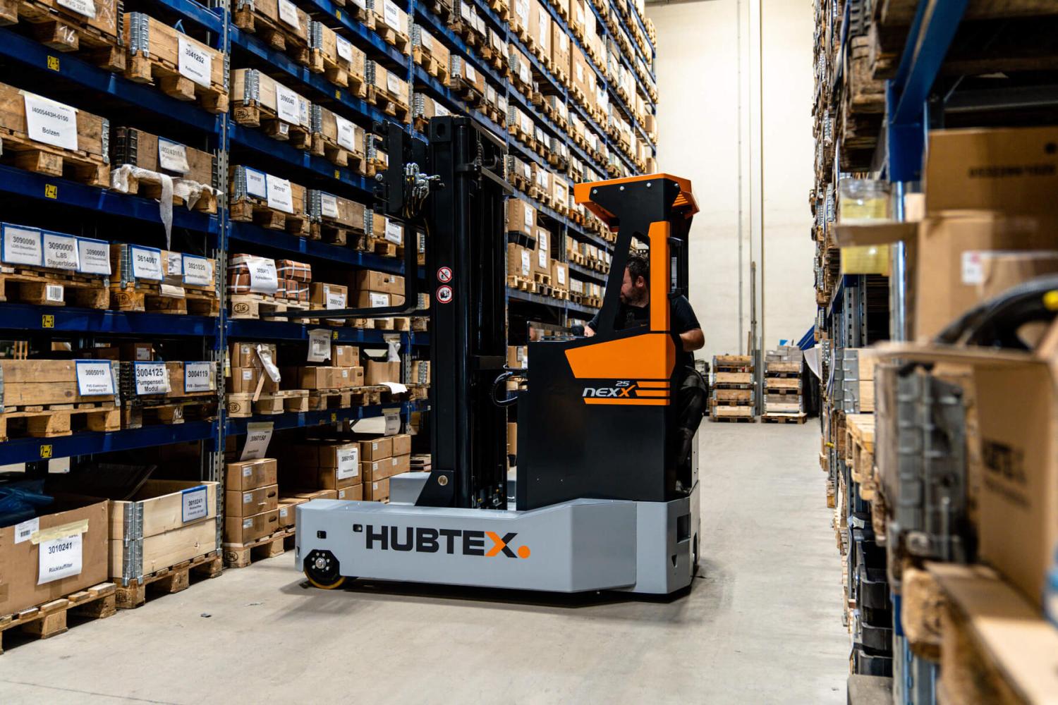 HUBTEX NexX 25 meerweg-schubmasttruck rijdt door smalle magazijngang met palletstellingen